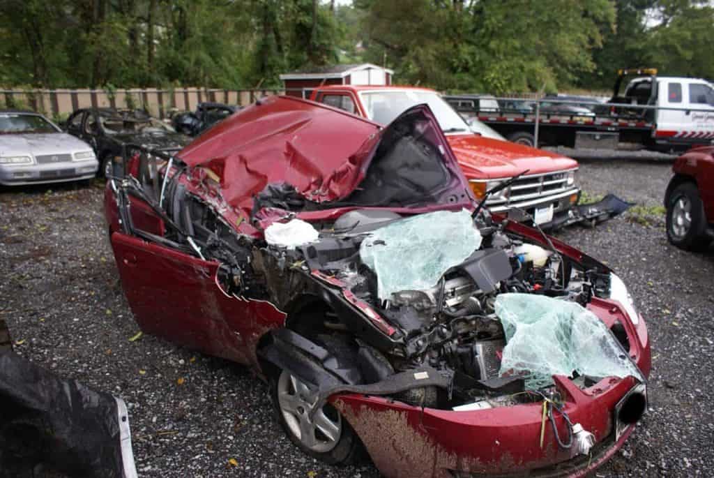 A red car with the roof completely crushed on the passenger side